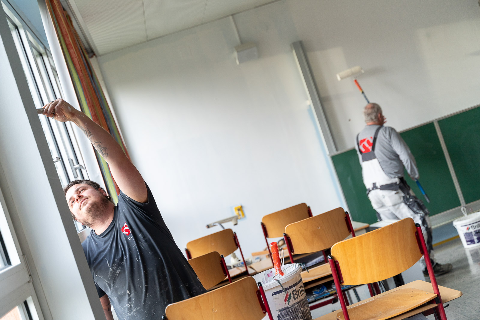  Zwei Mitarbeiter von Maler Merkle Illertissen führen Malerarbeiten in einer Schule aus und streichen die Wände professionell. 