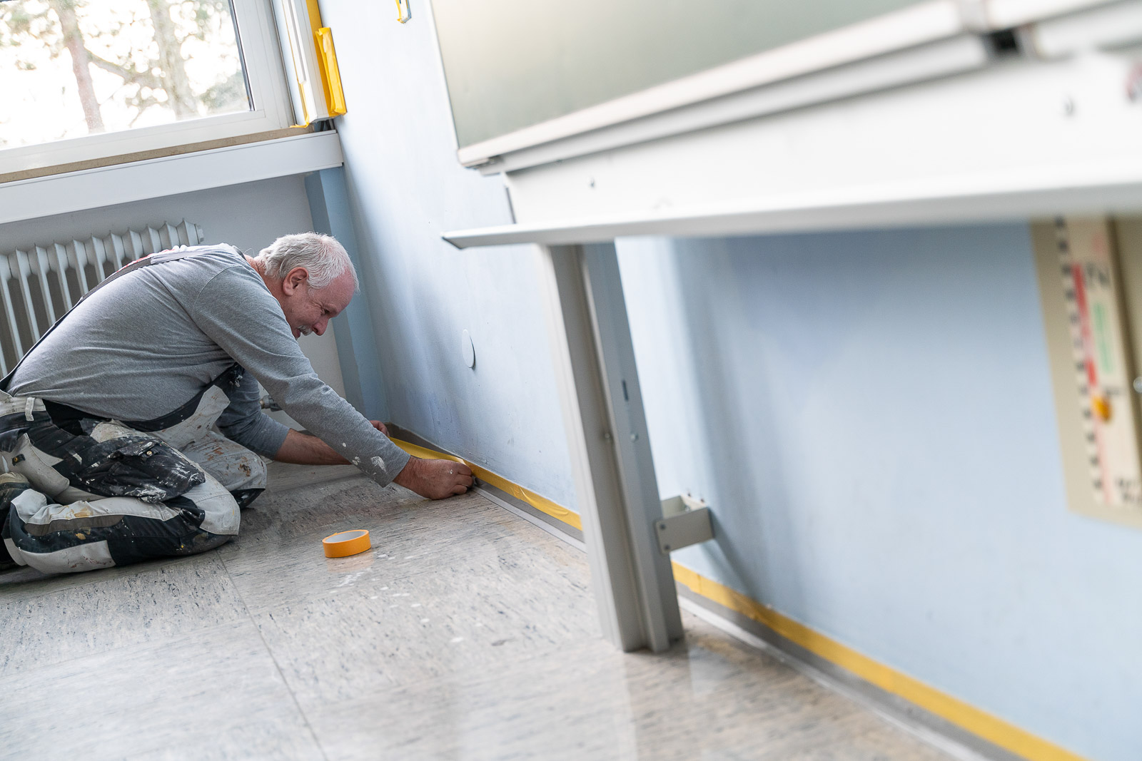  Ein Mitarbeiter von Maler Merkle Illertissen klebt eine Sockelleiste sorgfältig ab, um die Malerarbeiten vorzubereiten. 