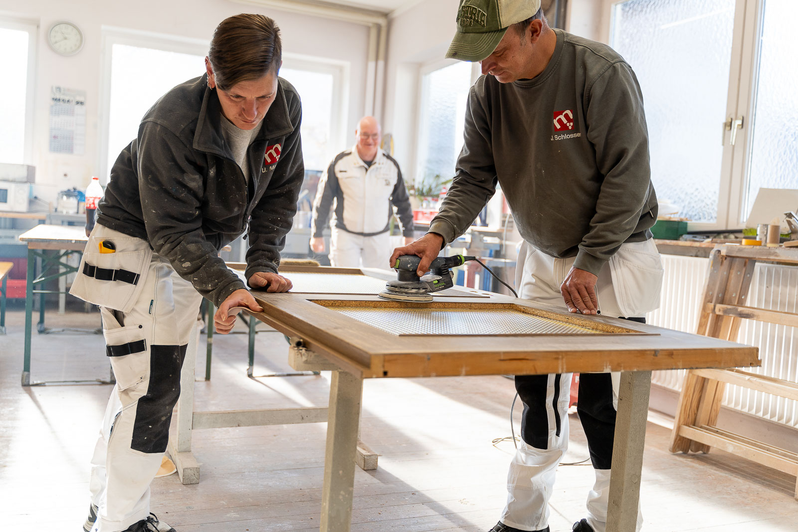  Zwei Mitarbeiter von Maler Merkle Illertissen schleifen eine Holztür fachgerecht im Rahmen von Zusatzleistungen. 